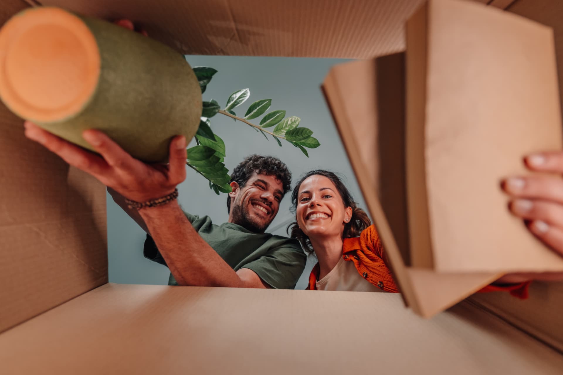 Couple souriant déballant un carton de déménagement, plante à la main